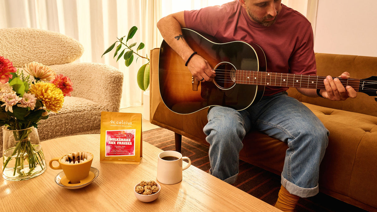 Guitariste qui boit un café et savoure un café de spécialité de 94 celcius avec un sac jaune sur la table
